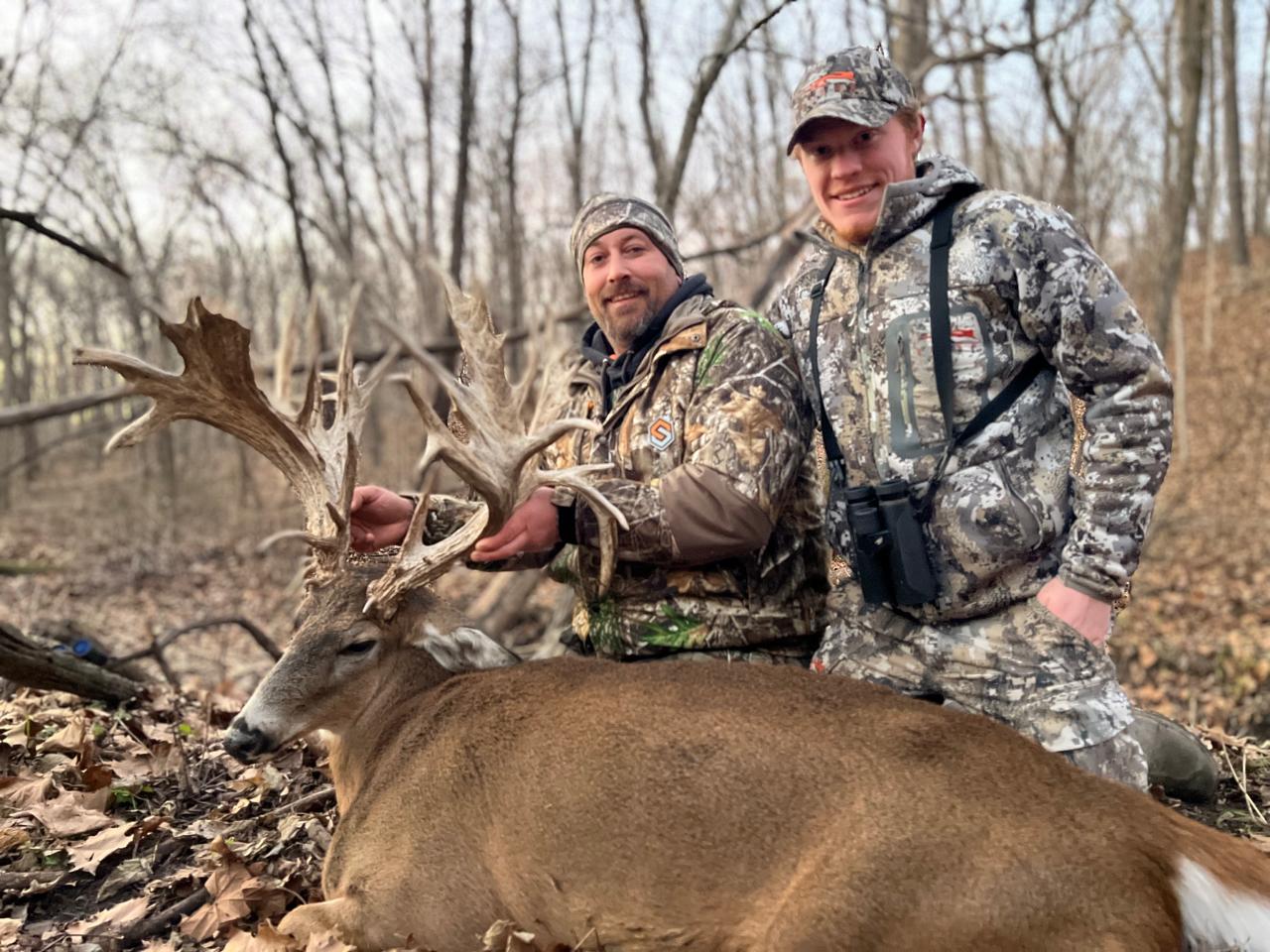 Two hunters kneeling beside a harvested whitetail buck
